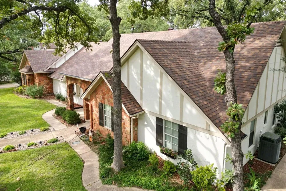 Tudor-style home under oak trees with a brown shingle roof